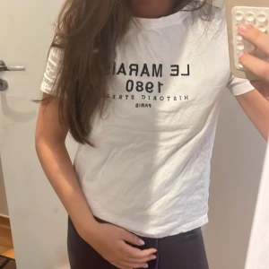 Zara tshirt  - Vit t-shirt med svart texttryck 'LE MARAIS 1980 HISTORIC STREET PARIS' på bröstet. Klassisk rund halsringning och korta ärmar. Modellen är rak och normal i passformen. Perfekt basic med fransk vibe.