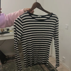 Randig långärmad tröja i bomull - Säljer en klassisk långärmad tröja med svarta och vita horisontella ränder. Tröjan har rund halsringning och är tillverkad i mjuk bomull, perfekt för lager-på-lager eller som den är. Enkel och tidlös stil som funkar året runt.