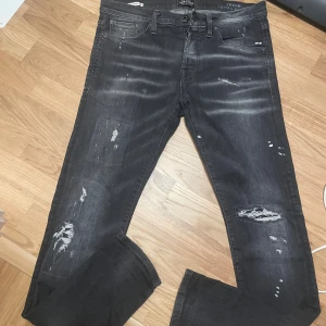 Svarta slim fit Glenn jeans med slitningar - Svarta slim fit Glenn jeans från Jack & Jones i storlek 31/32. Jeansen har snygga slitningar och lagade detaljer framtill, klassisk femficksmodell och normal midja. Materialet är jeans med en något stretchig känsla för extra komfort.