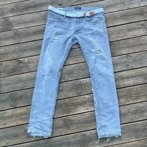 Grå jeans från Jack & Jones - Säljer mina Jeans ifrån Jack & Jones med riktigt feta slitningar, Jeansen sitter slim fit och har riktig bra passform, storlek W32, L32. Hör av er vid intresse & frågor.