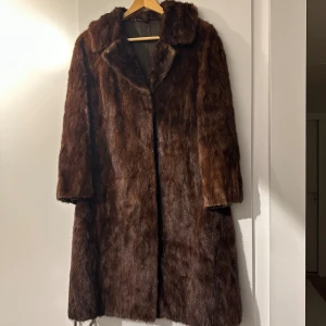 Brun pälsjacka med klassisk krage - Säljer en lång, brun pälsjacka med klassisk krage och rak passform. Perfekt för dig som vill sticka ut med en tidlös och lyxig look. Kappa i mink. Ingen storlek angiven men troligtvis en strl 38