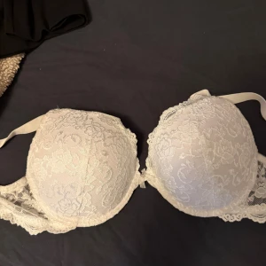 Vit spets-bh med blommönster - Säljer en vit bh med vacker spets och blommigt mönster. Bh:n har vadderade kupor och fina spetsdetaljer längs kanterna. Perfekt för dig som gillar romantisk och feminin stil.