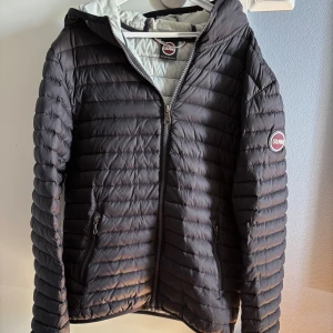 Colmar pufferjacka i svart - Säljer en svart pufferjacka från Colmar med huva och dragkedja framtill. Två fickor med dragkedja och Colmar-logga på ärmen. Jackan är i mycket gott skick. Storlek 166-170cm/14y.