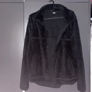 Svart teddyjacka med dragkedja - Mjuk och fluffig svart teddyjacka från 157 med hel dragkedja framtill och hög krage. Jackan har långärmade ärmar och en loose passform som ger en chill vibe. Perfekt för kalla dagar när du vill vara både bekväm och snygg. Använd 2 gånger säljer för den inte passar mig och är för stor