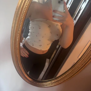 Vit blommig bandeau tubtopp - Säljer en söt vit bandeau tubtopp med små blommor i rosa och grönt. Toppen är ärmlös och croppad, perfekt för varma dagar. Materialet är ribbat och stretchigt för en tight passform. Superfin till jeans eller kjol!