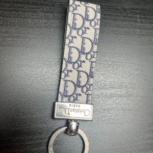 Christian Dior Paris Keychain - Elegant Christian Dior Paris nyckelring i canvas och metall med ikoniskt Dior-mönster. Mycket fint skick, inga synliga repor eller slitage. Perfekt accessoar för att hålla dina nycklar med stil och lyxig känsla.