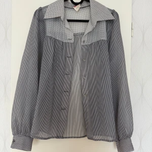 Randig och prickig blus med knappar - Snygg blus med tunna svarta och vita ränder samt prickigt mönster på krage och axelparti. Långärmad med breda manschetter och knappar framtill. Materialet är lätt och transparent, perfekt för dig som gillar unika detaljer och kontraster.den är genomskinlig:)