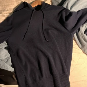 Mörkblå hoodie med huva och snörning - Snygg mörkblå hoodie med huva och snörning. Tröjan har ribbade muddar vid ärmslut och nederkant, vilket ger en skön passform. Perfekt för dig som gillar en enkel och stilren look. Materialet känns mjukt och bekvämt mot huden.