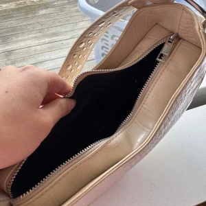 Beige väska - • Snygg beige axelväska med silvriga nitar. •Väskan har ett innerfack med dragkedja.