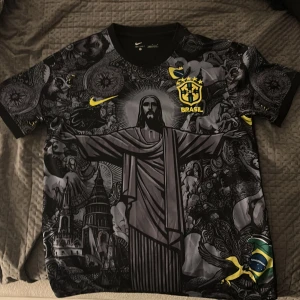 Nike Brasil fotbollströja svart/gul M - Unik Brasilien fotbollströja från Nike med svart och grått konstnärligt tryck, stora motiv av Kristusstatyn och brasilianska symboler. Broderat CBF-märke och Nike-logga i gult. Korta ärmar, lätt och ventilerande material.