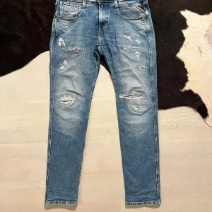 Replay Anbass slim fit jeans blå - Replay Anbass jeans i slim fit med slitna detaljer och hål på framsidan. Färgen är klassiskt ljusblå med tvättad look. Säljer pga för små och rensar garderoben. Skriv om ni har frågor!