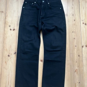 Svarta jeans från Sandro Paris - Svarta jeansbyxor från Sandro Paris i klassisk rak modell. Byxorna har fem fickor, silverfärgade nitar och en snygg svart färg. Tillverkade i bomull med en regular passform som sitter skönt och stilrent. Perfekta för dig som gillar en clean och tidlös look.