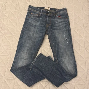 Slim Glenn jeans från Jack & Jones - Snygga blå jeans från Jack & Jones, modell Slim Glenn. Jeansen har en slim passform, klassisk femficksdesign och coola slitningar framtill. Gula kontrastsömmar och läderpatch bak. Perfekta för dig som gillar en smalare siluett.