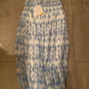 Blåvit boho långkjol med mönster - Säljer en boho-inspirerad långkjol från gina!146/152. Säljs inte längre! Aldrig använt! Prislapp finns på! Kjolen har ett blåvitt abstrakt mönster och bred resår i midjan för skön passform. Perfekt för dig som gillar avslappnad och trendig stil. Materialet är mjukt och lätt, vilket gör den bekväm att bära.