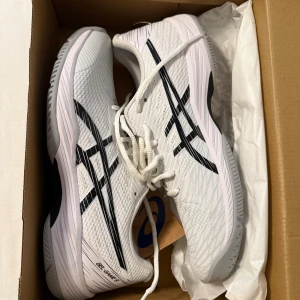 Asics Gel-Game 9 vita sneakers oanvända  - Snygga Asics Gel-Game 9 sneakers i vitt med svarta detaljer och klassisk Asics-logga på sidorna. Ovandelen är i ventilerande mesh och skon har snörning samt platt sula för bra grepp. Perfekta för dig som gillar sportig stil och vill ha bekväma skor till träning eller tennis. De är oanvända och i princip nya.