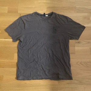 Brun t-shirt med tryck i flera språk - Snygg brun t-shirt i bomull med coolt tryck på både bröstet, ärmen och ryggen med ordet 'action' på flera olika språk. Klassisk rund hals och korta ärmar. Perfekt för dig som gillar unika och stilrena plagg med en twist.