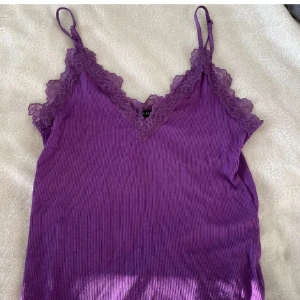 Lila ribbad linnetopp från Amisu - Säljer en lila ribbad linnetopp från Amisu med smala axelband och v-ringning. Toppen har fina spetsdetaljer längs urringningen och är tillverkad i ett mjukt, stretchigt material. Perfekt för att ge outfiten en färgklick! Står storlek M men passar mig som är S 