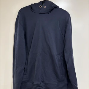 Marinblå hoodie från Armani - Snygg marinblå hoodie från Emporio Armani med silverfärgade detaljer och logotyp på huvan. Tröjan har långa ärmar, fickor på sidorna. Perfekt för dig som gillar stilrena och exklusiva plagg med cool branding. Endast använd 1 gång. Nyskick. 