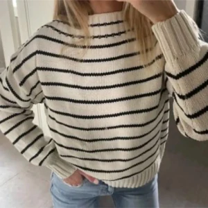 Randig stickad tröja i vit och svart - Säljer en snygg stickad tröja med horisontella svarta ränder på vit botten. Tröjan har en rund hals, långa ärmar och ribbade muddar. Perfekt för dig som gillar en chill och stilren look till jeans eller kjol.