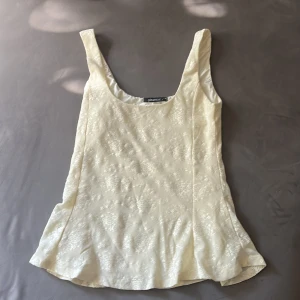 Blommig vit linnetopp från Gina Tricot - Säljer en ljusvit linnetopp från Gina Tricot i storlek M. Toppen har ett subtilt blommigt mönster i tyget och är ärmlös med breda axelband och rundad halsringning. Materialet har en lätt glansig finish som ger en elegant känsla.