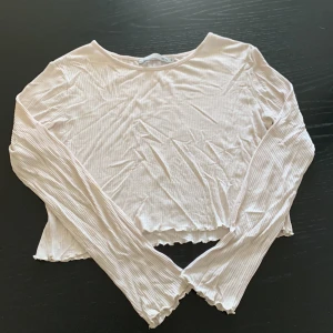 Ljusbeige ribbad långärmad topp 157 - Supersöt ljusbeige långärmad topp från 157 med ribbad struktur och volangkant vid ärmslut och nederkant. Croppad modell som ger en trendig vibe, perfekt att styla med höga jeans eller kjol. Mjuk och stretchig i bomullsmix för extra komfort.