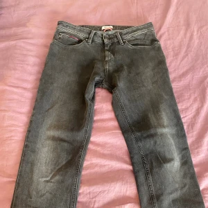Svarta jeans från Hilfiger Denim - Säljer ett par svarta jeans från Hilfiger Denim med klassisk femficksdesign och diskret logga på bakfickan. Jeansen har en rak passform och är tillverkade i mjukt denimtyg med lätt tvättad look. Perfekta för dig som gillar stilrena och tidlösa jeans.