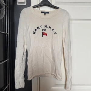 Vit långärmad tröja från Gant - Vit långärmad tröja från Gant . Tröjan är i mjukt stickat material. Den sitter lite figursytt. De finns en liten fläck på sidan (se bild 4) men den syns knappt. Skriv för mer info💕