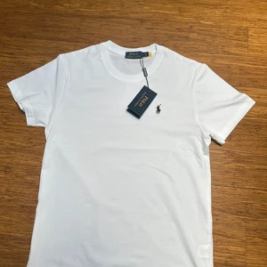 Vit t-shirt från Polo Ralph Lauren - Klassisk vit t-shirt från Polo Ralph Lauren med rund hals och liten broderad logga på bröstet. T-shirten är i mjuk bomull och har en clean look som passar till allt. Perfekt basic-plagg för garderoben.
