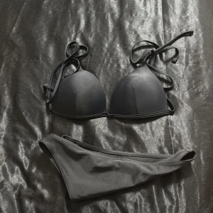 Svart bikini med knyt - Snygg svart bikini med vadderad trekants-bh och knytband i nacken och ryggen. Klassiska bikinitrosor i matchande svart. Perfekt för stranden eller poolen, enkel och stilren design.