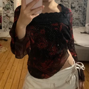 Blommig svart och röd meshblus - Säljer en transparent svart blus med röda blommor och glittriga detaljer. Jag köpte den i vietnam så vet inte stl eller märke men den passar s-m, aldrig använd