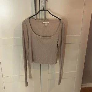Beige ribbad långärmad topp H&M - Säljer en beige ribbad långärmad topp från H&M med croppad passform och bred, rundad halsringning. Toppen är i mjukt material och har en stilren look som är enkel att matcha med jeans eller kjol. Perfekt för dig som gillar minimalistisk stil.