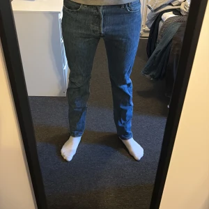 Levi's 501 blå jeans straight fit - Klassiska blå Levi's 501 jeans med rak passform och normal midja. Jeansen har fem fickor, knappgylf och är tillverkade i slitstarkt bomullsdenim. Perfekta för dig som gillar en tidlös och clean look.