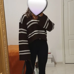 Brun randig croppad stickad tröja - Säljer en brun stickad tröja med vita och svarta ränder. Tröjan är croppad med breda, långa ärmar och avslappnad passform. Perfekt för dig som gillar en chill och trendig stil.