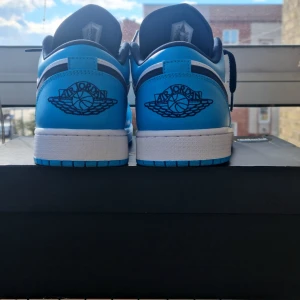 Air Jordan 1 Low (blå/vit) - Nästan nya!  - 🔥 Säljer ett par exklusiva Air Jordan 1 Low i blå/vit färg, i nästan nyskick – de har bara använts vid max 3 tillfällen.  ✅ Storlek: enligt bild (passar perfekt för dig som gillar klassisk AJ1-fit). ✅ Skick: både sulor och läder är i riktigt fint skick, inga större spår av användning. ✅ Komplett paket: kommer i originalkartong + verifieringslapp från Restocks, samt ett extra par snygga blåa skosnören (ej original).  Passar lika bra för samlare som för dig som vill lyfta din outfit med