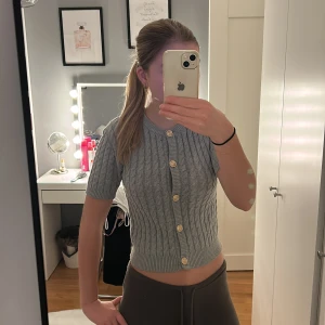 Grå kabelstickad kofta från H&M - Superfin grå kabelstickad kofta från H&M med kort ärm och snygga guldknappar framtill. 💗skriv om du har några frågor💗                         Finns på flera sidor