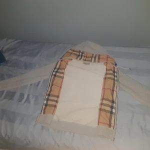 Grå hoodie från Burberry Xs-S 165-180 - Säljer en snygg grå hoodie från Burberry med klassiskt rutigt foder i huvan. Tröjan har dragkedja framtill, två fickor och en broderad logga på bröstet. Perfekt för dig som gillar stilrena och exklusiva plagg med en twist.