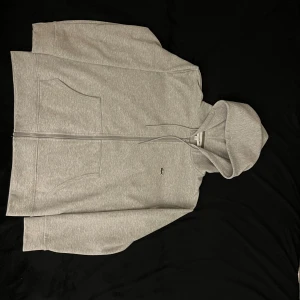 Grå hoodie från Lacoste med dragkedja - Grå zip hoodie från Lacoste. Har använts i ungefär 1 år och tyckte det var dags att sälja den pågrund av att det inte är min stil längre. Det enda som inte finns är skötseletikett. Jag är 177 och tycker att den passar bra !OBS pris går att diskuteras!