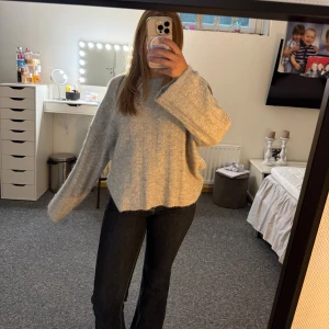 Ljusgrå stickad oversized tröja - Mysig ljusgrå stickad tröja med breda ärmar och avslappnad oversized passform. Tröjan har en enkel rund halsringning och är tillverkad i ett mjukt, fluffigt material som känns riktigt skönt mot huden. Perfekt för kyliga dagar och enkel att styla.