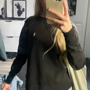 Svart långärmad tröja från Polo Ralph Lauren - Svart långärmad tröja från Polo Ralph Lauren med klassisk vit broderad logga på bröstet. Enkel och stilren design, rund halsringning och mjukt material som känns skönt mot huden. Perfekt för dig som gillar en clean och tidlös look.