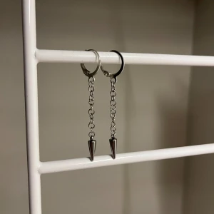 Silvriga kedjeörhängen med spets - Säljer ett par coola örhängen i silverfärgad metall med kedjor och spetsiga hängen. Perfekt för dig som gillar edgy och minimalistisk stil. Örhängena har en enkel ring som fäste och hänger snyggt från örat. Handgjort