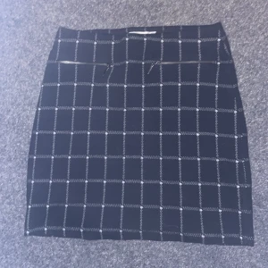 Svart rutig kortkjol från Esprit - Snygg svart kortkjol från Esprit med vitt rutmönster och två små dragkedjor framtill. Kjolen har en rak passform och är gjord i ett mjukt material  med resorband i midjan. Classy & perfekt för att klä upp sig.