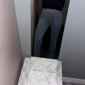 Ljusblå velourbyxor Juicy Couture XS - Ljusblå mjukisbyxor från Juicy Couture i velour med snörning i midjan, stora fickor fram och bakficka med knapp. Klassisk broderad Juicy-logga på ena benet. Perfekt för en chill och trendig look.