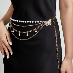 Guldigt kedjebälte med pärlor och fjäril - Snyggt guldigt kedjebälte med flera lager kedjor, vita pärlor och en detalj i form av en fjäril. Bältet har hängande pärlor och passar perfekt för att ge din outfit en extra touch. Stilren och trendig accessoar som verkligen sticker ut.