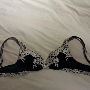 Marinblå spets-bh från Intimissimi - Snygg marinblå bh från Intimissimi med vacker vit spetsdetalj i blommigt mönster över kuporna och längs kanten. Justerbara axelband och elegant design som ger en lyxig känsla. Perfekt för dig som gillar stilrena underkläder med det lilla extra.