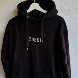 Odz merch ”ZUBBI”  storlek M - Svart hoodie från ODZ med vit broderad logga på bröstet. Klassisk modell med huva, snörning och känguruficka. Mjuk bomullskänsla och ribbade muddar vid ärmslut och nederkant. Perfekt för chill dagar eller streetstyle. Storlek: M