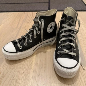 Svarta Converse All Star high-top - Klassiska svarta Converse All Star high-top sneakers i skinn med vita gummisulor och tåhätta. Skorna har grå snörning, rund tå och tydlig logga på sidan. Perfekta för dig som gillar en tidlös och cool stil.