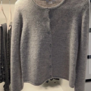 Grå kofta från Gina Tricot - Mysig grå kofta från Gina Tricot med rund halsringning och knappar hela vägen framtill. Långärmad och i ett fluffigt, stickat material som känns både trendigt och bekvämt. Perfekt att slänga på sig när det är kyligt ute.