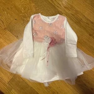 Vit och rosa blommig kortklänning - Supersöt vit och rosa kortklänning med långärmade ärmar och blommigt mönster på bröstet. Klänningen har ett lager av tunn tyll och dekorativa blommor med band i midjan. Lite noppar de bild #74cm #9-12 månader 