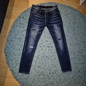 Unika jeans Alessandro Zavetti - Snygga limited edition mörkblå jeans från Alessandro Zavetti med slimfit passform och slitna detaljer på benen. 'Born in Italy'-patch bak. Jeansen har diskreta vita färgstänk och är tillverkade i stretchig denim för skön komfort.