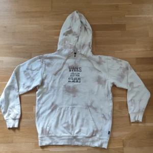 Vans tie-dye hoodie med tryck - Säljer en beige och ljusbrun tie-dye hoodie från Vans med stor tryckt solblomma och texten 'Vans 1966' på ryggen. Framsidan har tryck och känguruficka. Mjuk bomullsmix, huva med snörning och långa ärmar.